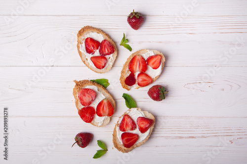Toasts or bruschetta with strawberries on cream cheese on white wooden background. Top view. Copy space