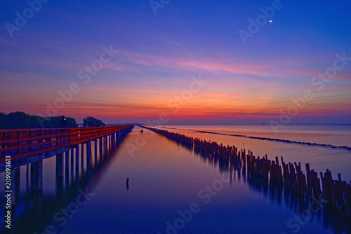Fishermen leave fishing while the twilight is on and the crescent moon still shines at wooden red bridge over the sea. © Kanchanaphum