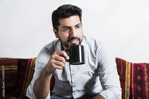 Smiling man sit on sofa and drink cup of coffee © pavelgulea