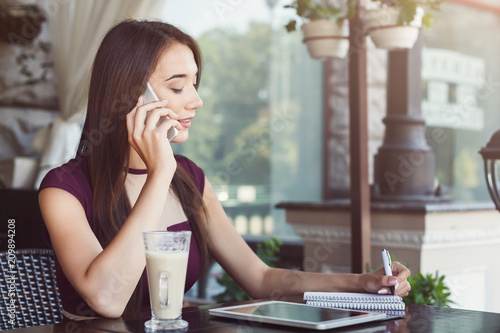 Young businesswoman talking on smartphone and making notes