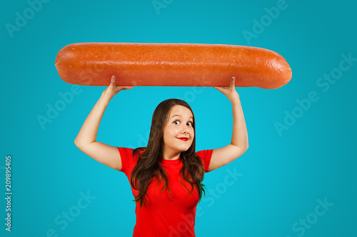 Cute funny young girl holds over herself huge sausage on a blue background