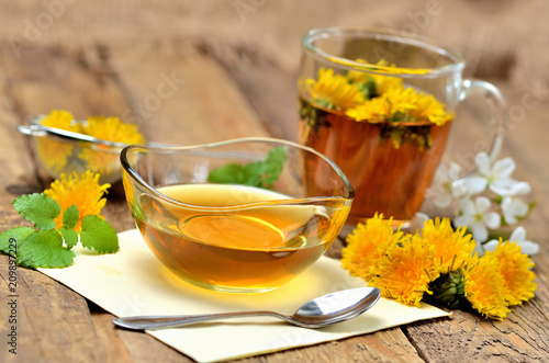 Dandelion honey, herbal tea, spring flower, spoon, fresh mint leaves and dandelion head around