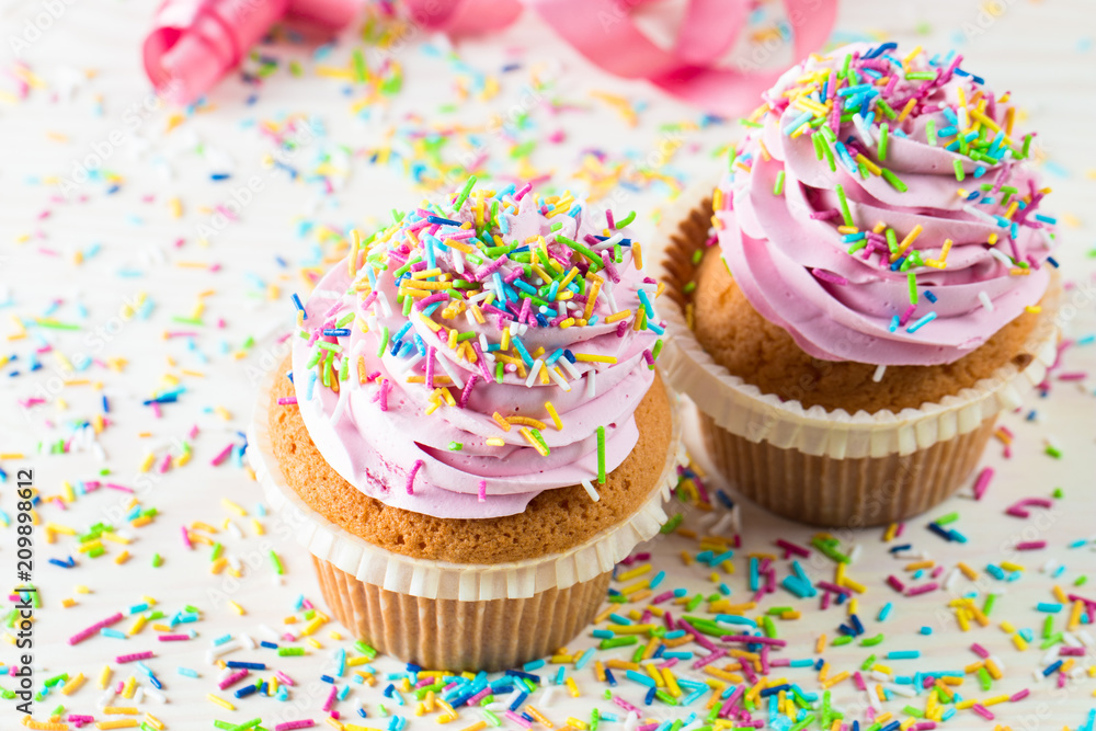 Closeup of cupcakes with vanilla, berries, pink and white cream, chocolate and sprinkles on wooden background. Selective focus. Sweet dessert tasty food concept muffin. Closeup of cupcakes with vanilla, berries, pink and white cream, chocolate and sprinkles on wooden background. Selective focus. Sweet dessert tasty food concept muffin.