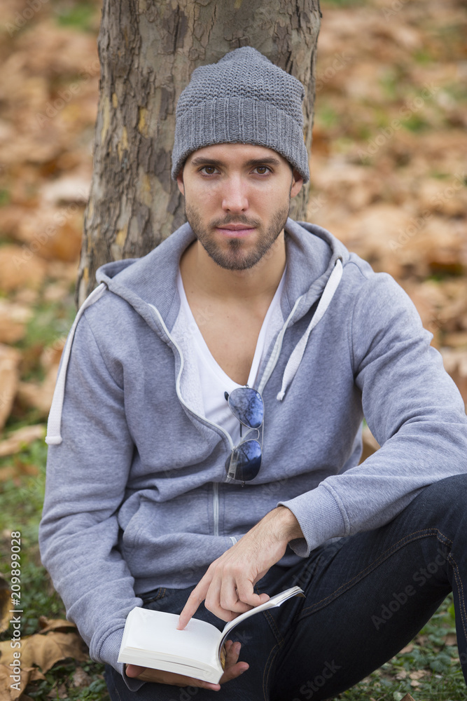 Obraz premium Handsome man in nature reading a book. Autumn leaves. Copy space