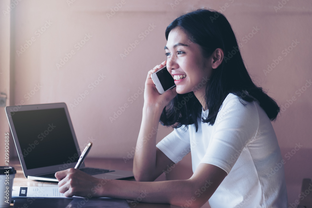 Happy businesswoman talking on mobile while working on laptop at her desk in office Happy businesswoman talking on mobile while working on laptop at her desk in office