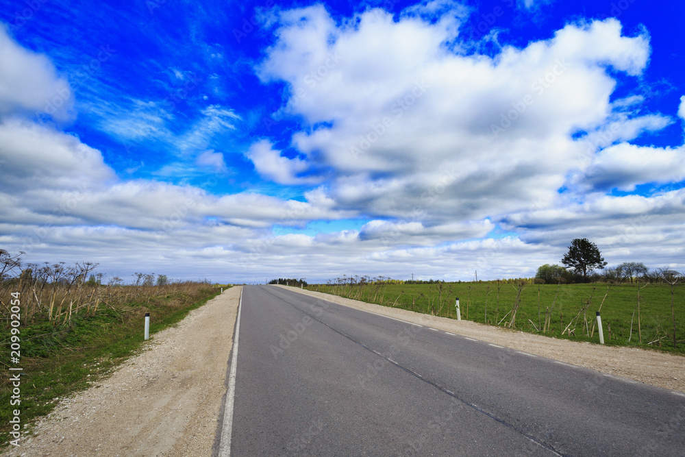 Asphalt highway in countryside with gravel shoulders on both sides and cloudy blue sky as background