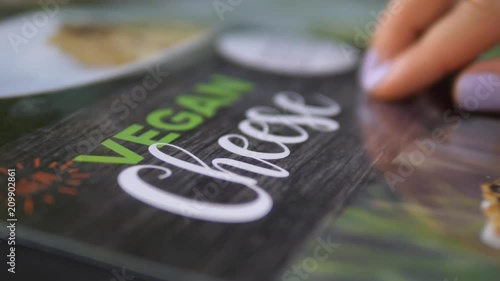 Woman Finger Points At Food Menu With Vegan Cheese Dish. Closeup. 4K. photo