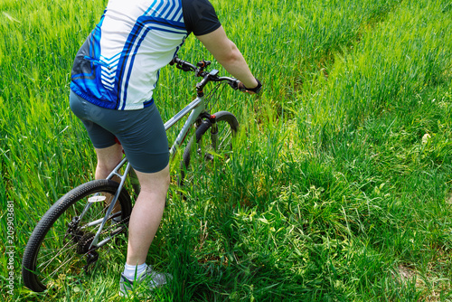 young strong man riding bicycle by green field