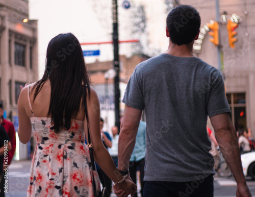 A couple walking down the street together from behind hand in hand.
