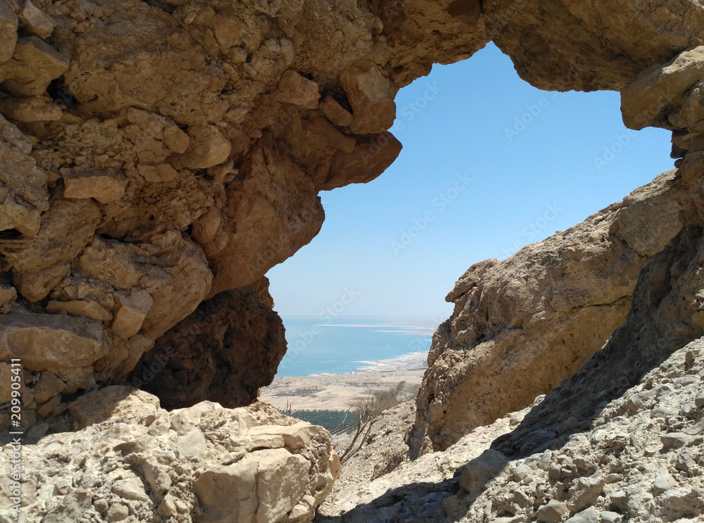 The sandstone arc in mountains. Dead Sea and its coastline are visible through it. The sky is clear and blue. The day is hot and sunny. There is Israel.