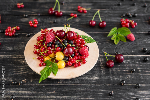 Raspberry, cherry, red currant, blackcurrant on a wooden plate against a dark background. It can be used as a background