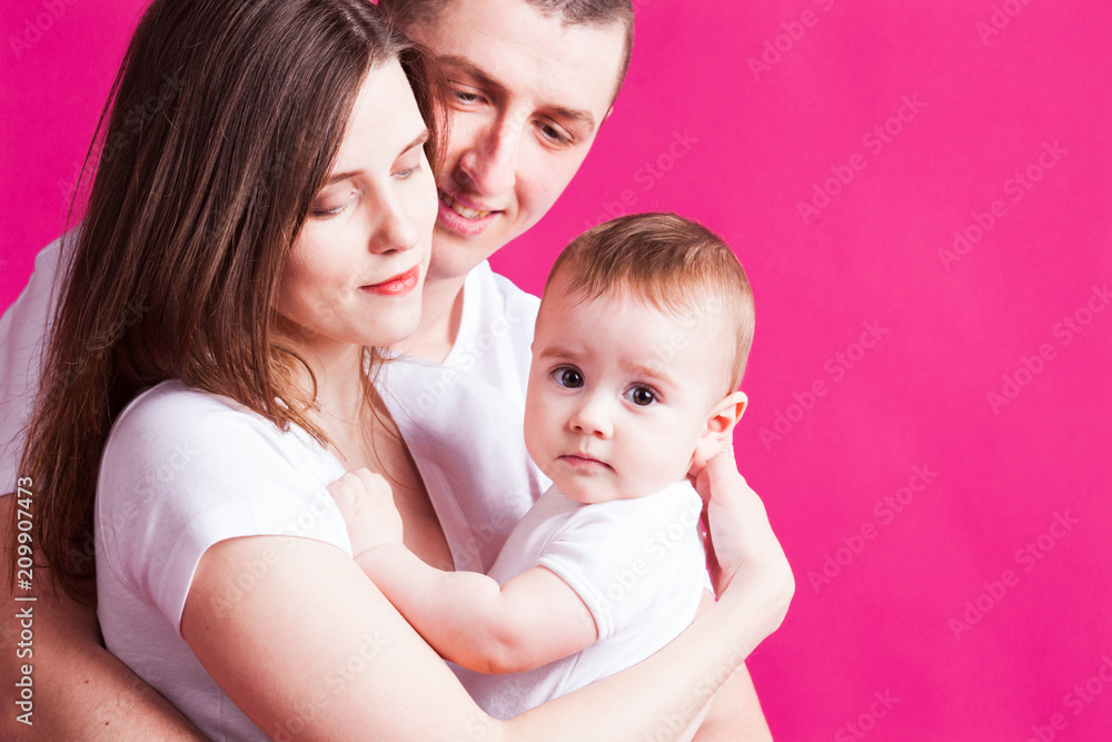 Beautiful family is posing with their infant, pink background Beautiful family is posing with their infant, pink background