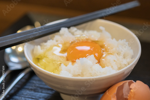 Close up of Tamago Kake Gohan - Raw egg on rice in white bowl with chopstick and spoon. Famous Japanese traditional breakfast food. photo