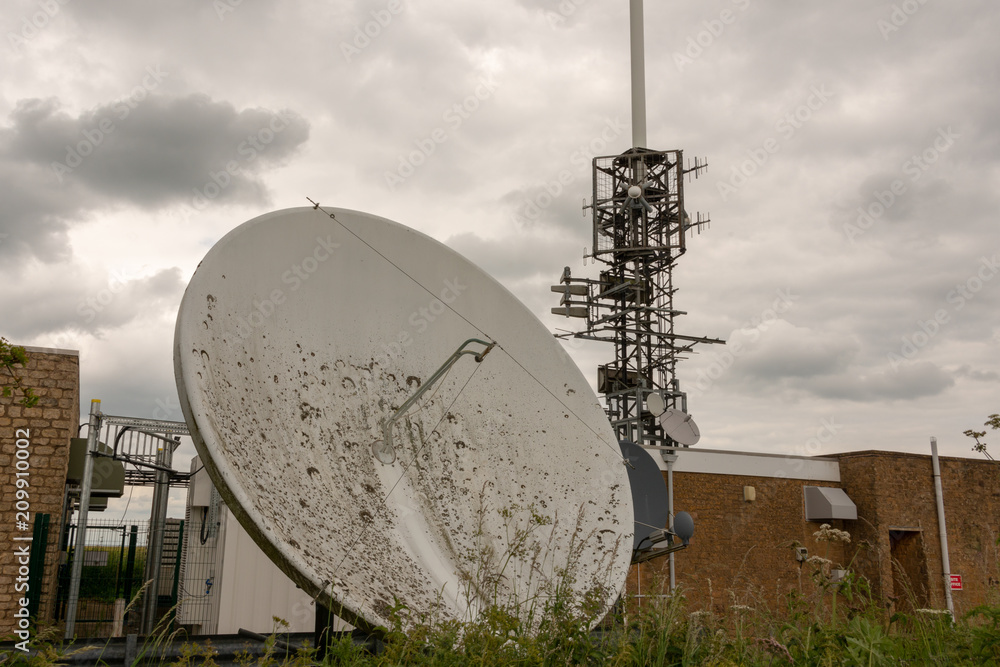 old cell phone communications tower  and large dirty overgrown satellite dish