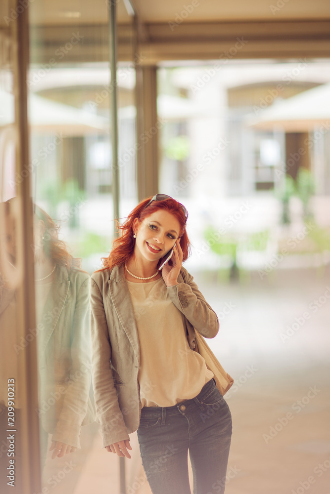 Fototapeta premium Beautiful young woman in the city, mall is busy with her mobile phone, talking, smiling