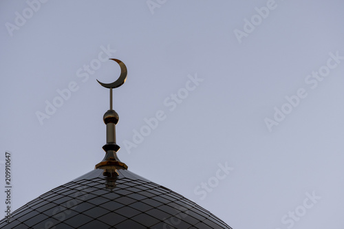 The symbol of Islam is a golden crescent moon on top of the mosque minaret on the blue evening of the morning sky.