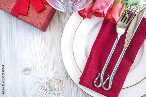 Festive table setting with bouquet of red roses and gift box on light wooden background with copy space photo