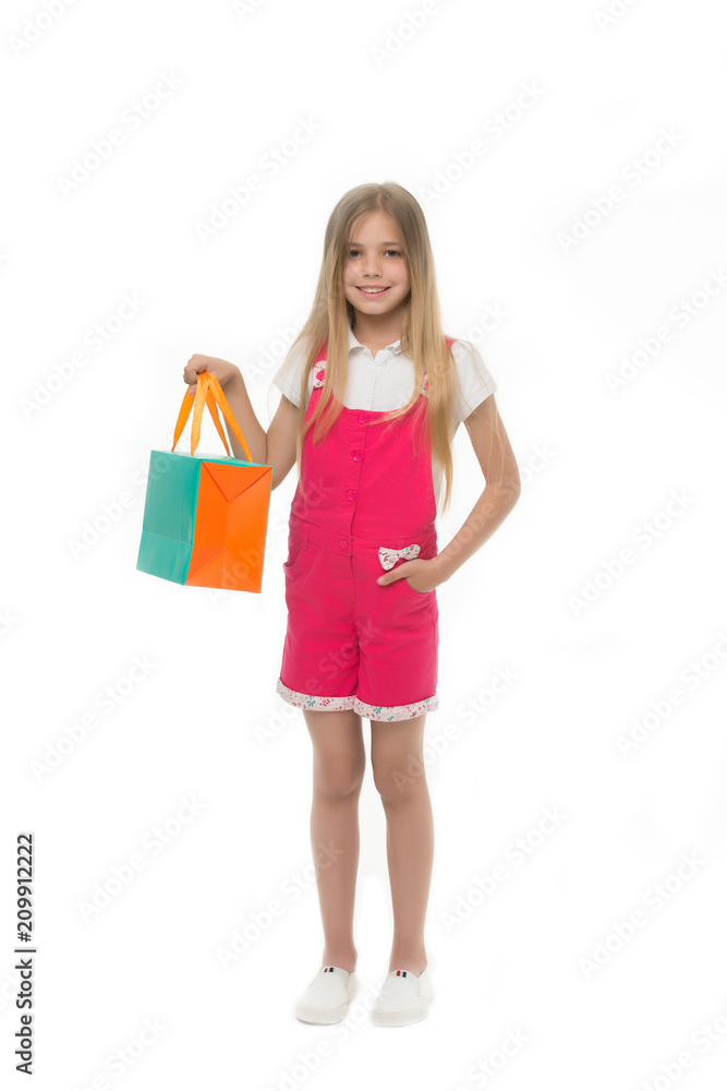 Little shopaholic. Child buy modern items in mall. Girl smiling happy face carries shopping bag package, isolated white background. Kid girl long hair likes shopping. Shopping addicted concept
