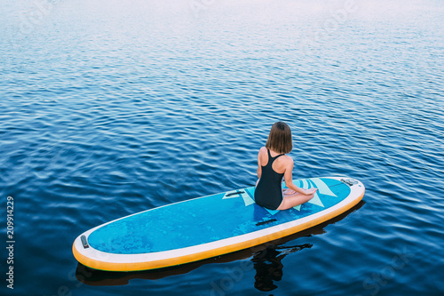 Young woman meditating on paddle board. practice yoga on paddle board, woman sitting on paddle board, at sea, view from above