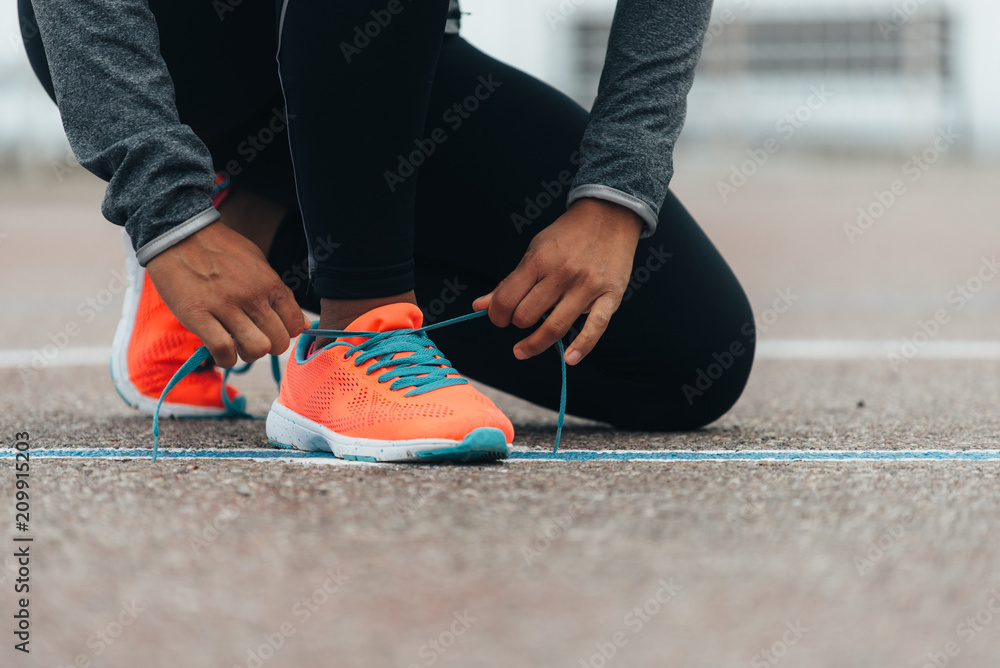 Detail of sporty swman lacing running shoes before before training. Outdoor city workout concept. Female fitness athlete getting ready for working out. - obrazy, fototapety, plakaty 