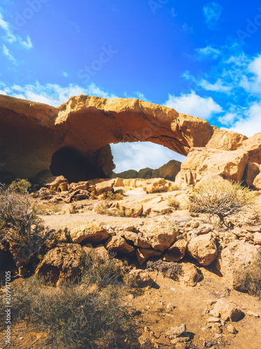 Rocky landscape with volcanic stone forming natural monuments. Natural stone arch with clouds on the horizon.