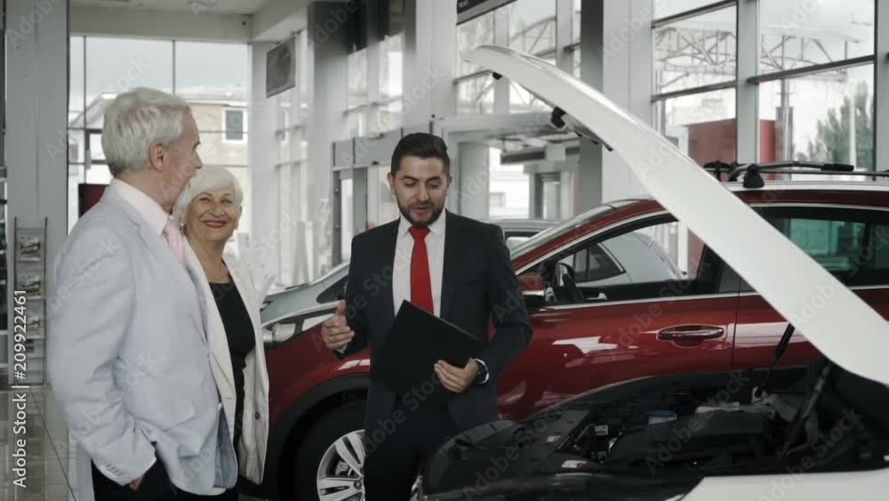 Senior couple at the car salon are choosing a car with the sales assistant. Happy customers at the auto salon. Senior couple at the car salon are choosing a car with the sales assistant. Happy customers at the auto salon.