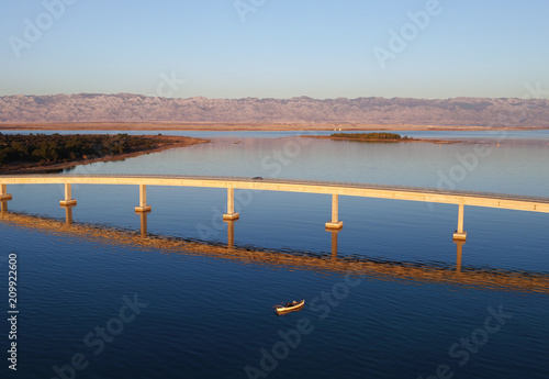 Bridge to island Vir with beautiful reflection in the sunset with boat and mountain range Velebit, Adriatic sea (Jadransko more), Croatia, drone aerial shot
