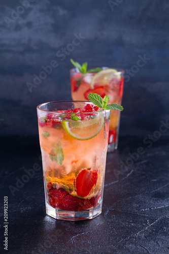 Strawberry mojito cocktail with berries, lime and mint. Summer berry cocktail on black background. vertical