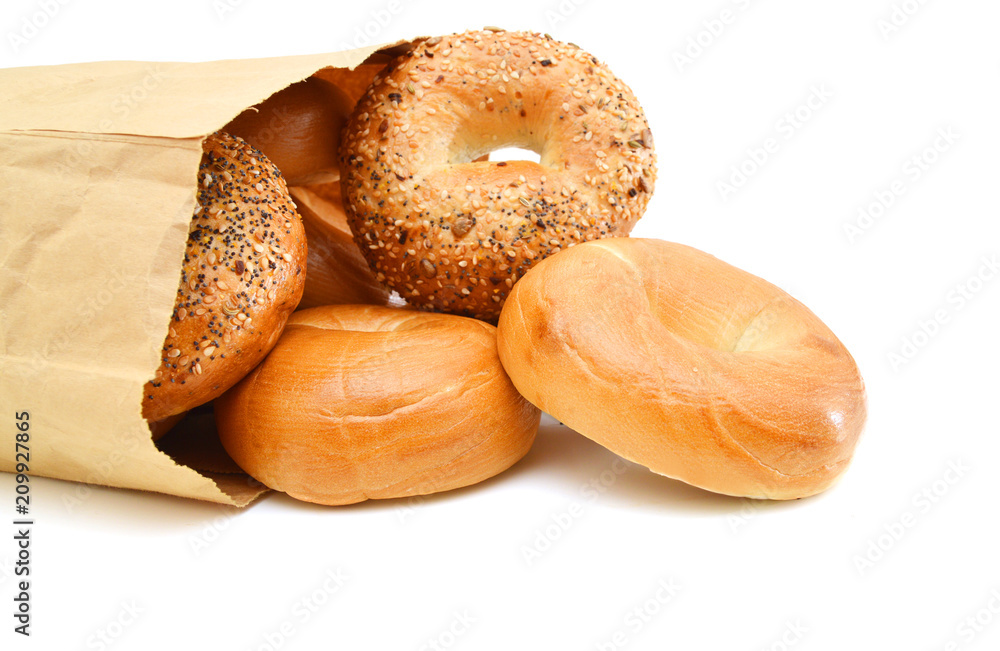Closeup of bagels in a brown paper bag laying on its side. Horizontal format on white with