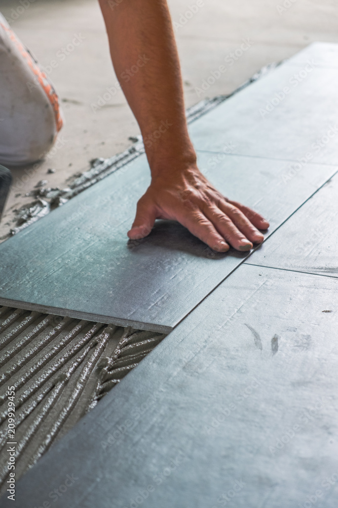 Worker's hands pressing ceramic floor tiles laid on applied adhesive Worker's hands pressing ceramic floor tiles laid on applied adhesive