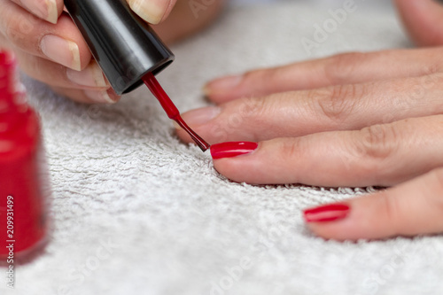 Woman painting her finger nails with red nail enamel on white towel in the bathroom