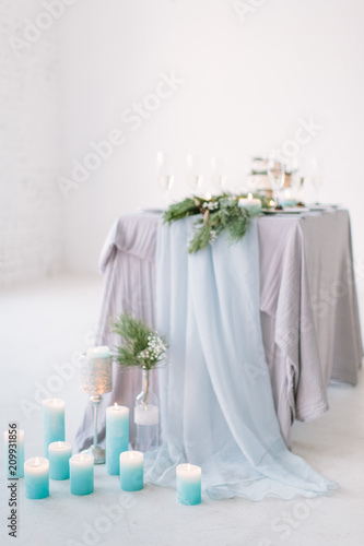 The composition of pine decoration suspended on the ceiling, candles, flowers and greenery standing on served table in the area of wedding party