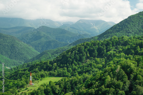 the antenna of the radio telephone connection stands on a glade in the mountains in the thick of the trees on a bright summer sunny day