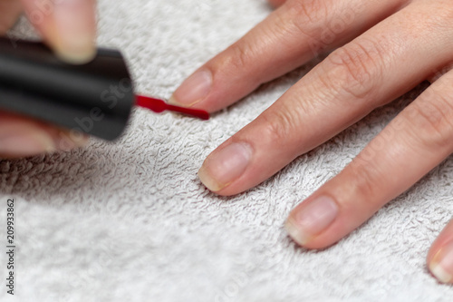 Girl lacquering her finger nails with red nail enamel on a white towel