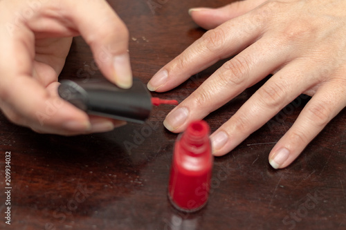 Nailcare with red finger nail enamel in front of dark wooden table