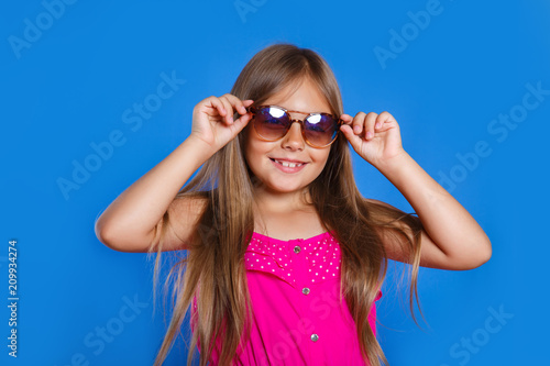 Portrait of young pretty girl in pink dress, sunglasses and hat on blue background . Summer vacation and travel concept © Elena Kratovich