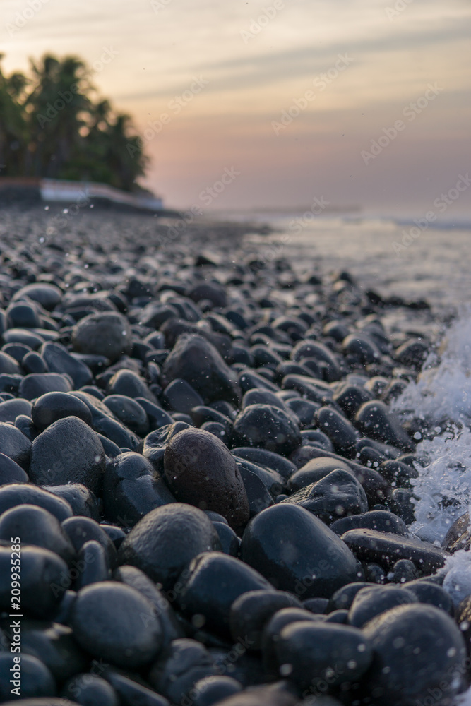 Obraz premium Ocean splash with a lot of foam on dark rocks at sunrise.