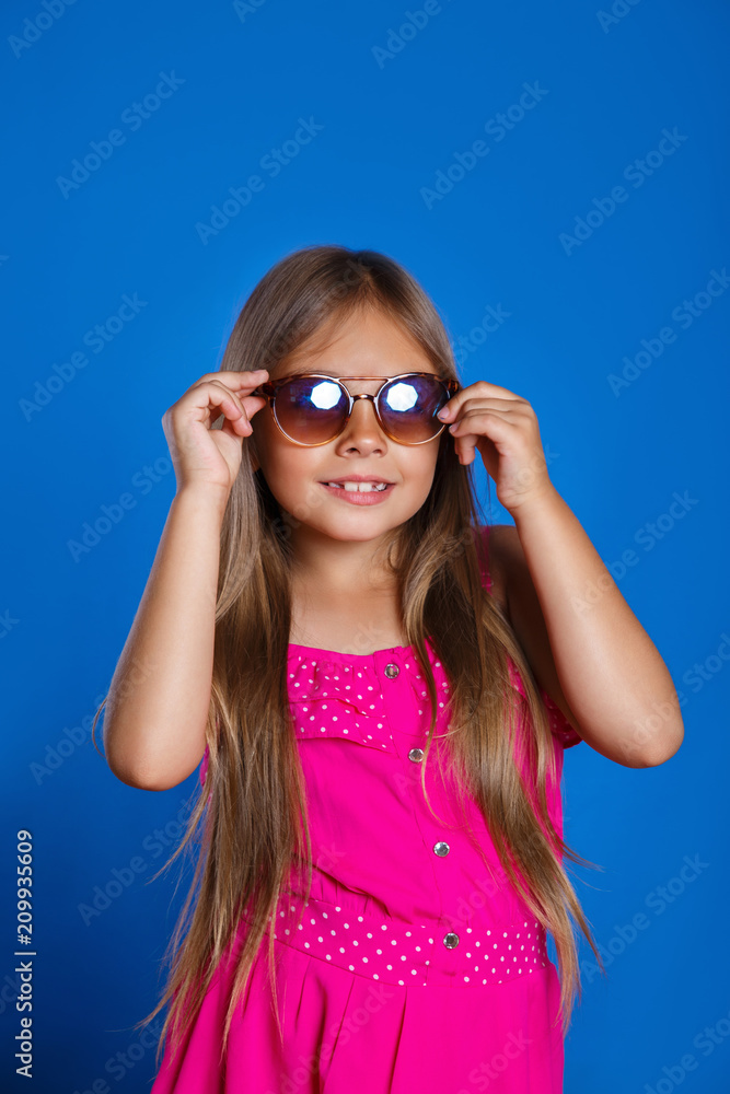 Portrait of young pretty girl in pink dress, sunglasses and hat on blue background . Summer vacation and travel concept Portrait of young pretty girl in pink dress, sunglasses and hat on blue background . Summer vacation and travel concept