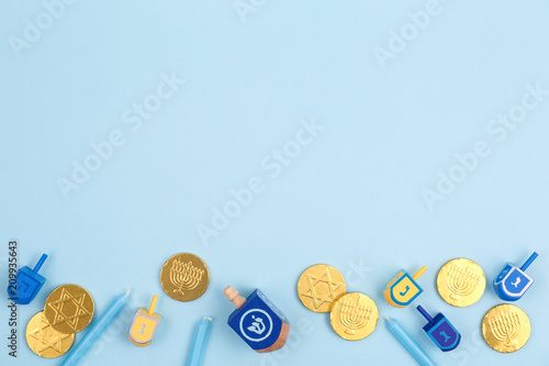 Blue background with multicolor dreidels, menora candles and chocolate coins. Hanukkah and judaic holiday concept.