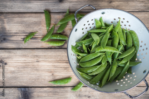 sugar snap peas in a white colander on a wooden table photo