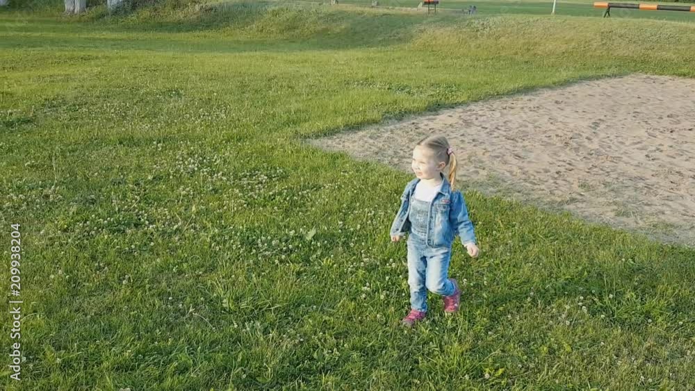 a little girl in denim clothes running in the Park on the sand. a little girl in denim clothes running in the Park on the sand.