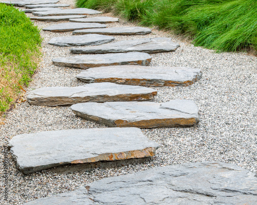 simple flat stone pathway on gravel surrounded by bright green grass in a Japanese garden