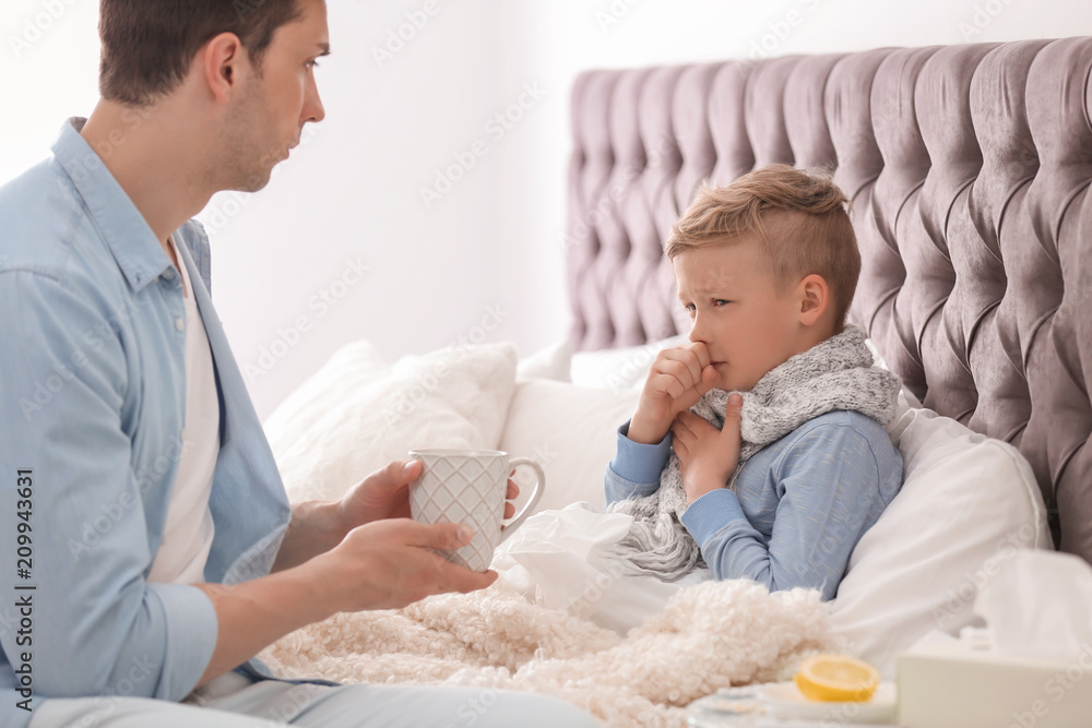 Father taking care of little son suffering from cold in bed Father taking care of little son suffering from cold in bed