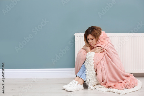 Canvas Print Sad woman suffering from cold on floor near radiator