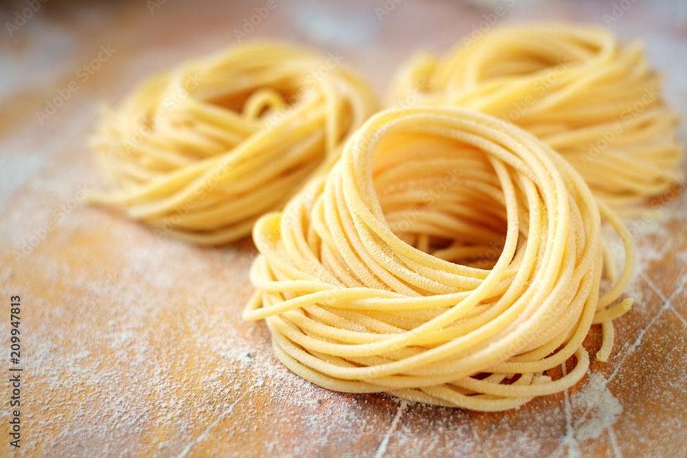 raw homemade spaghetti nest with flour on a wooden table. fresh Italian pasta - obrazy, fototapety, plakaty 