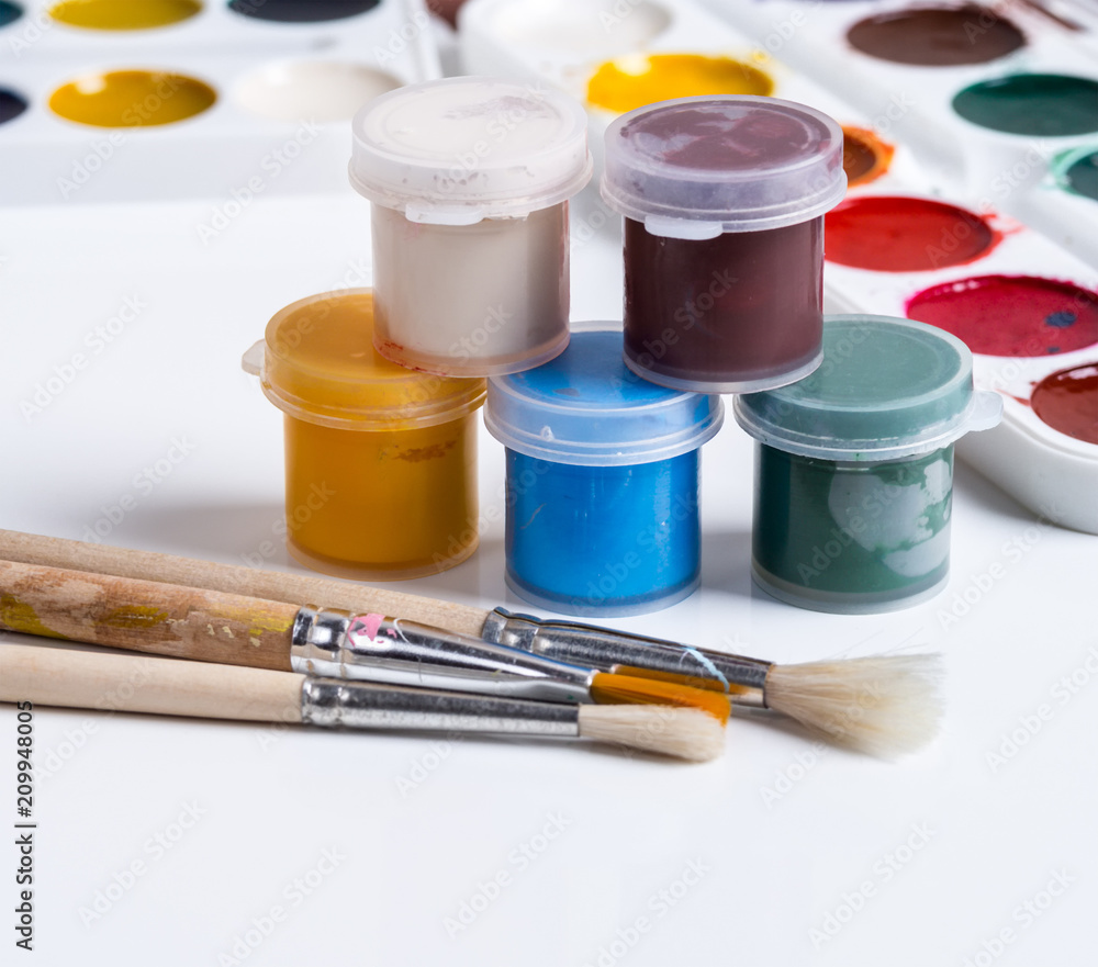 Gouache in jars, brushes and watercolors on a white background Gouache in jars, brushes and watercolors on a white background