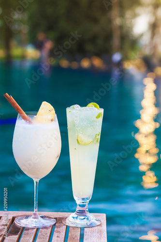 two perfect cocktails pina colada and mojito, pool background