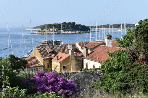 Sunny panoramic view over the rooftops of authentic Croatian houses which all welcome tourists in summer in Hvar isle old town. Paklinski islands and old fashioned tourist party boat at the background
