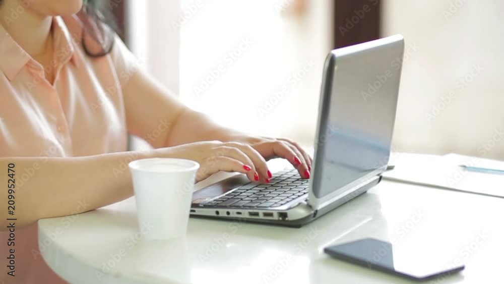 A woman is sitting in a cafe drinking coffee and working on a laptop. slow mo. The camera moves to dolly from the right to the left. A woman is sitting in a cafe drinking coffee and working on a laptop. slow mo. The camera moves to dolly from the right to the left.