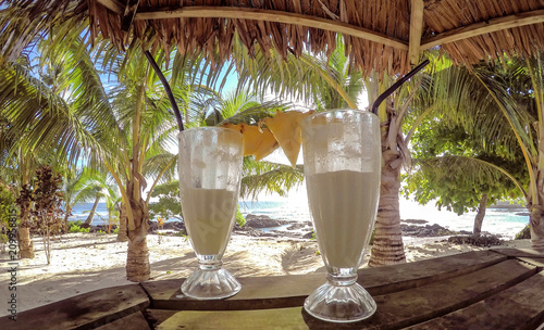 Half full glasses of tropical pina colada cocktail drink with pineapple garnish in glass with straws at exotic beach with thatched roof at Lefaga, Upolu Island, Samoa, South Pacific photo